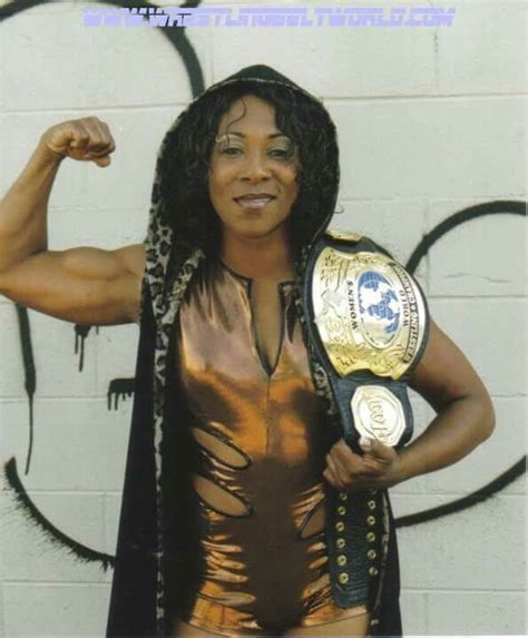 A Woman Posing In Front Of A Wall With A Wrestling Belt On Her Chest