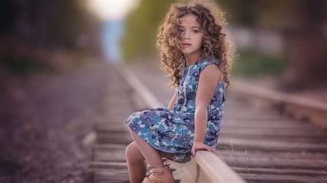 Curly Hair Cute Little Girl Is Sitting On Railroad Wearing Flower