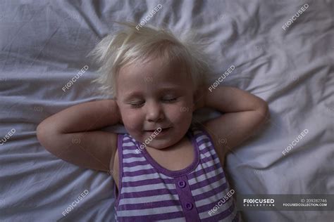 Toddler Girl Sleeping With Hands Behind Head On Bed In Bedroom