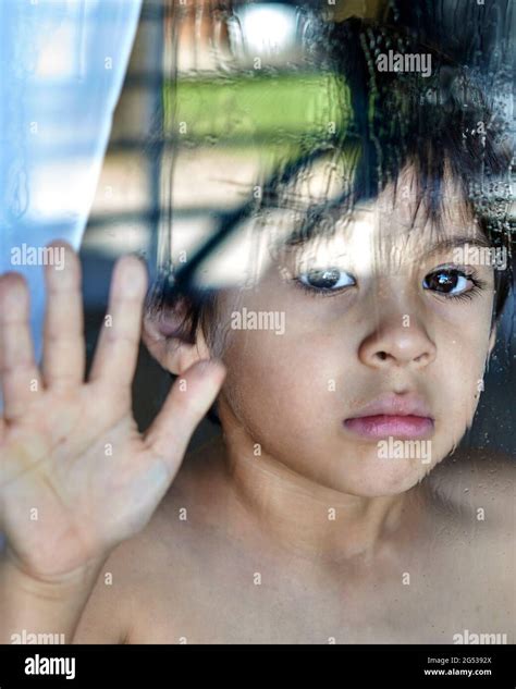 Title Sad And Anguished Child Looking Behind The Wet Glass With Hand