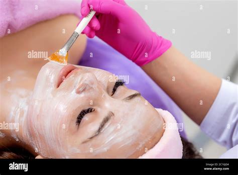 Beautician Makes A Face Clay Mask Against Acne On The Face Of A Woman To Rejuvenate The Skin