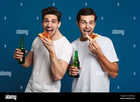 Excited Unshaven Two Guys Eating Pizza While Drinking Bear Isolated Over Blue Background Stock