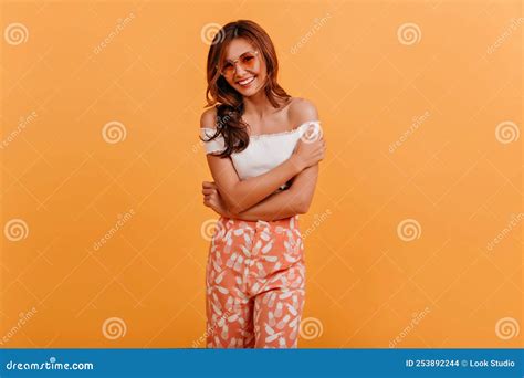 Indoor Portrait Of Modest Lady With Sweet Smile Girl With Wavy Long Hair Hugs Her Shoulders And