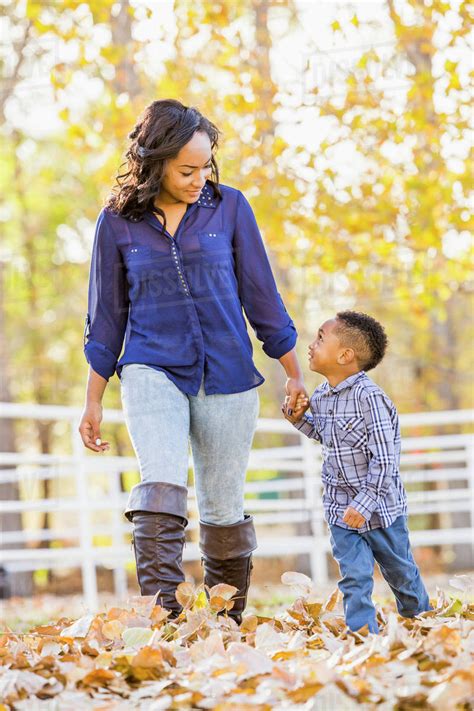 Black Mother And Son Holding Hands In Autumn Leaves