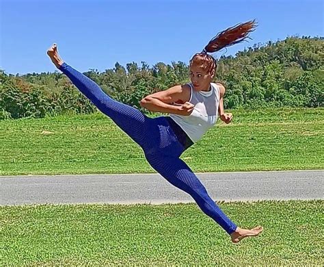 A Woman In Blue Tights And White Shirt Doing A Kick With Her Leg Up
