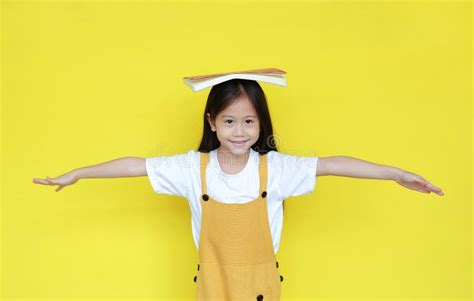 Asian Child Girl With Book On Head Isolated On Yellow Background