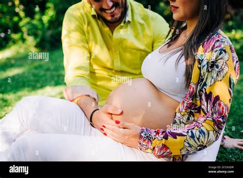 Husband Touching Stomach Of Pregnant Wife While Sitting In Park Stock