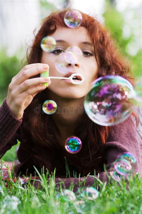 A Woman Laying In The Grass Blowing Bubbles On Her Face And Looking At