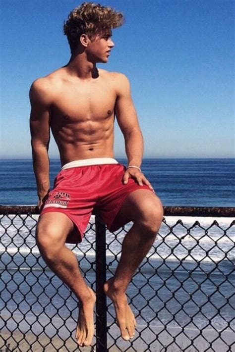 A Shirtless Man Leaning On A Fence By The Ocean With His Legs Crossed