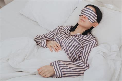 Calm Serene Young Woman Wear Striped Pajamas And Sleeping Mask Resting In Comfortable White Bed