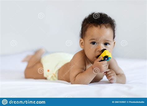 Cute African American Infant Baby Lying In Bed And Biting Toy Stock