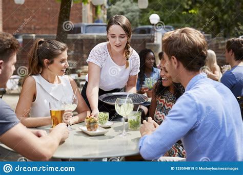 Waitress Serving Drinks To Group Of Friends Sitting At Table In Pub Garden Enjoying Drink ...