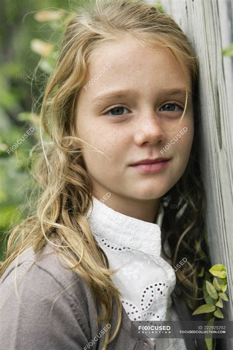 Portrait Of Dreamy Blonde Little Girl Leaning On Fence In Garden