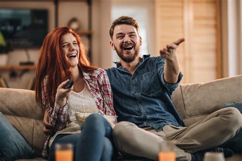 Young Couple Laughing While Watching Tv At Home Stock Photo Download