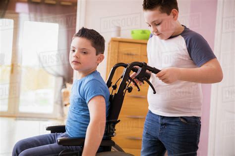 Boy Pushing Brother With Down Syndrome In Wheelchair Stock Photo