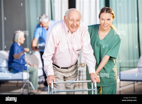 Female Caretaker Helping Senior Man In Using Zimmer Frame Stock Photo
