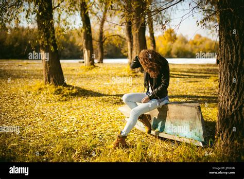 slim girl in blue jeans brown jacket and boots sat on the upturned boat on the shore yellow