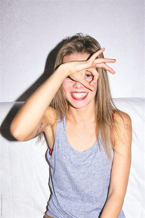 Smiling Young Woman Looking At Camera Through Hole Made By Fingers Del Colaborador De Stocksy