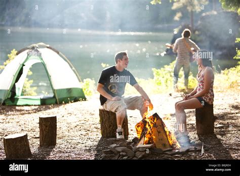Young Adults Camping Sit Around A Fire Next To A Lake In Idaho Stock