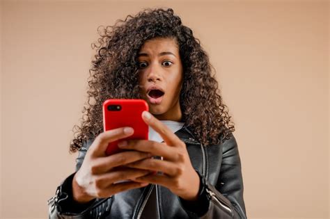 premium photo shocked surprised black girl looking at her phone screen isolated over brown