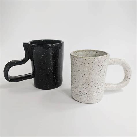 Two Black And White Coffee Mugs Sitting Next To Each Other On A White