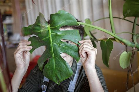 Premium Photo A Young Girl Covers Her Face With Green Leaf For Fun And Relax Home Plants On