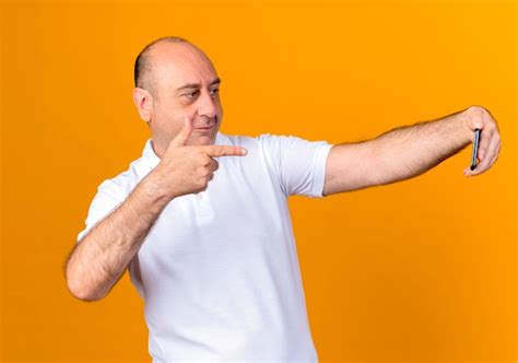 Free Photo Pleased Casual Mature Man Take A Selfie And Points At Phone Isolated On Yellow Wall