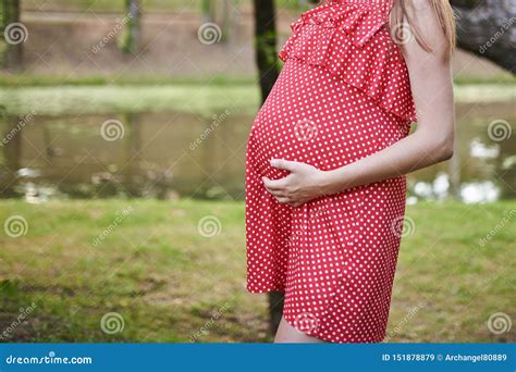 Belly Of A Pregnant Woman In Red In A White Polka Dot Dress With Her