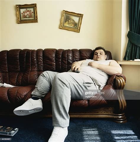 Overweight Young Man Falls Asleep While Lying On A Sofa Watching Tv