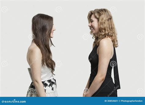 Two Female Friends Looking At Each Other And Smiling Over Gray