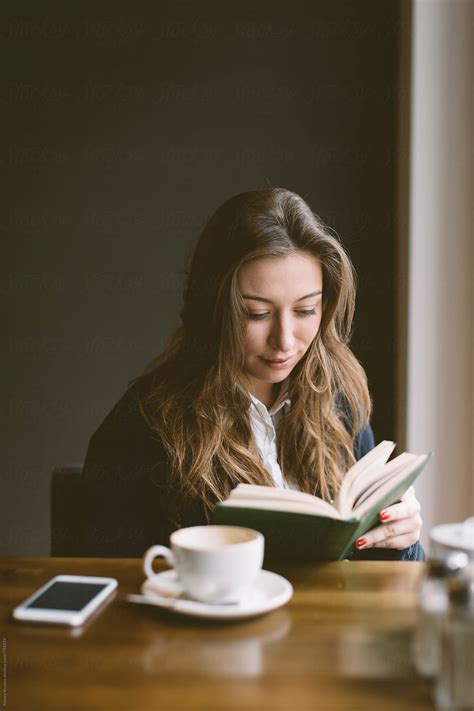 Young Woman Sitting In A Coffee Shop And Reading A Book Del