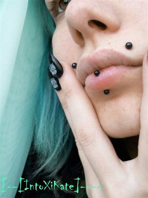 A Woman With Blue Hair And Piercings Holding Her Hands To Her Face