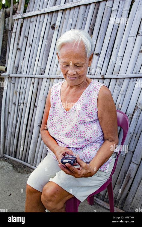 Senior Elderly White Haired Filipino Asian Woman Sitting Outdoors Trying To Use Her Smartphone