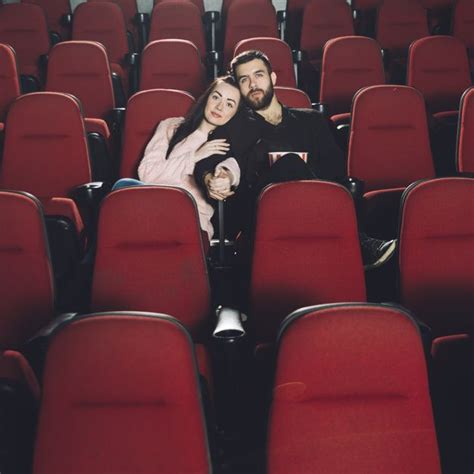 A Man And Woman Sitting In The Middle Of Rows Of Red Chairs With Their