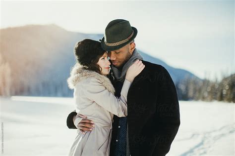 Young Mixed Couple Embrace In Love On Snow Covered Winter Lake By