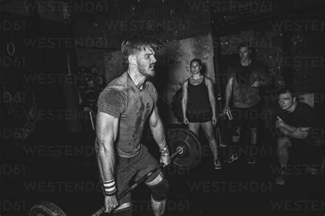 Cross Training Athletes Observing Man Lifting Barbell In Gym Stock Photo