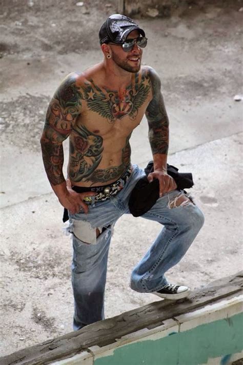 A Man With Tattoos On His Chest And Jeans Standing Next To A Skateboard Ramp