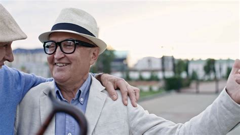 Two Retired Male Friends In Hats Hugging Each Other