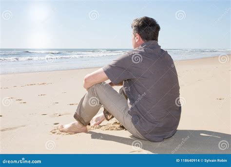 Handsome Man Thoughtful And Sitting On The Beach Watching Sea Ocean