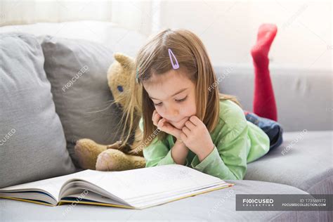 Little Girl Lying On Couch And Reading Book — Lying On Front Teddy