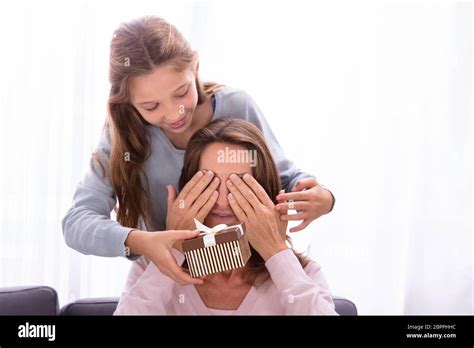Close Up Of Girl Giving Surprise T To Mother Covering Her Eyes Stock