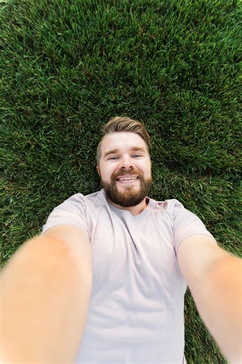 Young Man With Beard And Fashion Hair Style Lying On Grass Taking