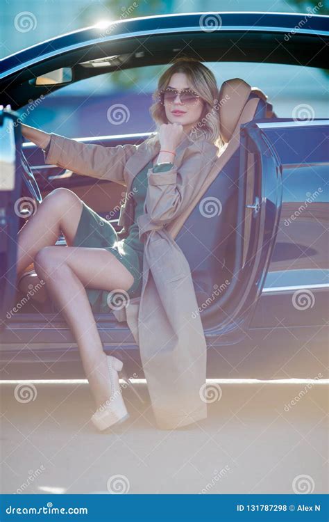 Image Of Woman With Glasses And Long Dress And High Heels Shoes Sitting In Car With Open Door