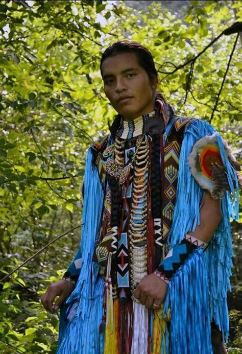 A Native American Man Standing In Front Of Some Trees
