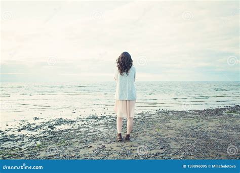 Beautiful Girl Standing Alone On The Coastline Of The Sea And Looking