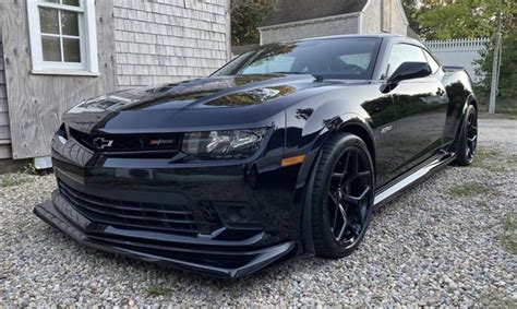 A Black Chevrolet Camaro Is Parked In Front Of A House With Gravel And