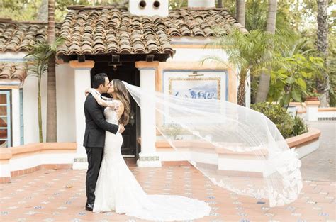 A Bride And Groom Standing In Front Of A Building With A Veil Blowing