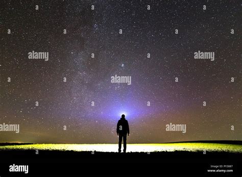 Back View Of Man With Head Flashlight Standing On Green Grassy Field