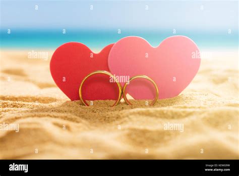 Close Up Of A Two Hearts With A Wedding Rings On Sandy Beach Stock
