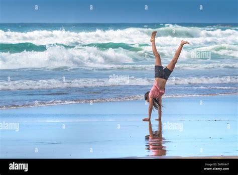A Young Teenage Girl Performing A Handstand On The Shoreline On Fistral